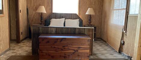 Un dormitorio con paneles de madera, una cama, dos lámparas de noche y un ventanal.
