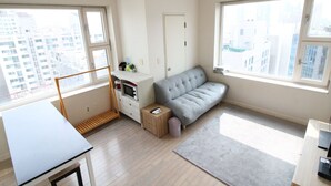 Un apartamento moderno con sofá, una mesita y un escritorio. Amplias ventanas ofrecen vistas de la ciudad.