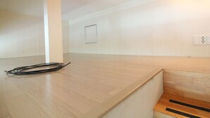 Una habitación con piso de madera, pared blanca con un interruptor de luz y un cable negro enrollado en el suelo.
