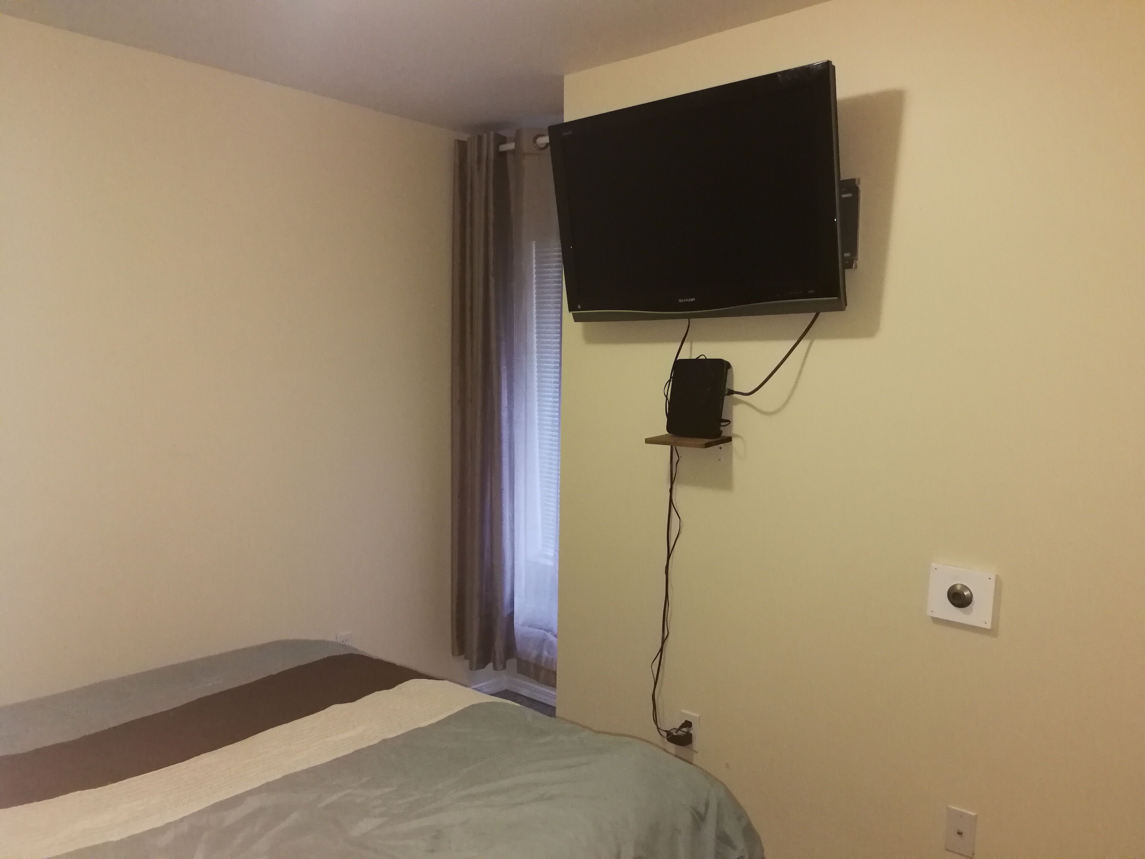 Une chambre à coucher avec un lit, un téléviseur fixé au mur et une prise électrique sur le mur.