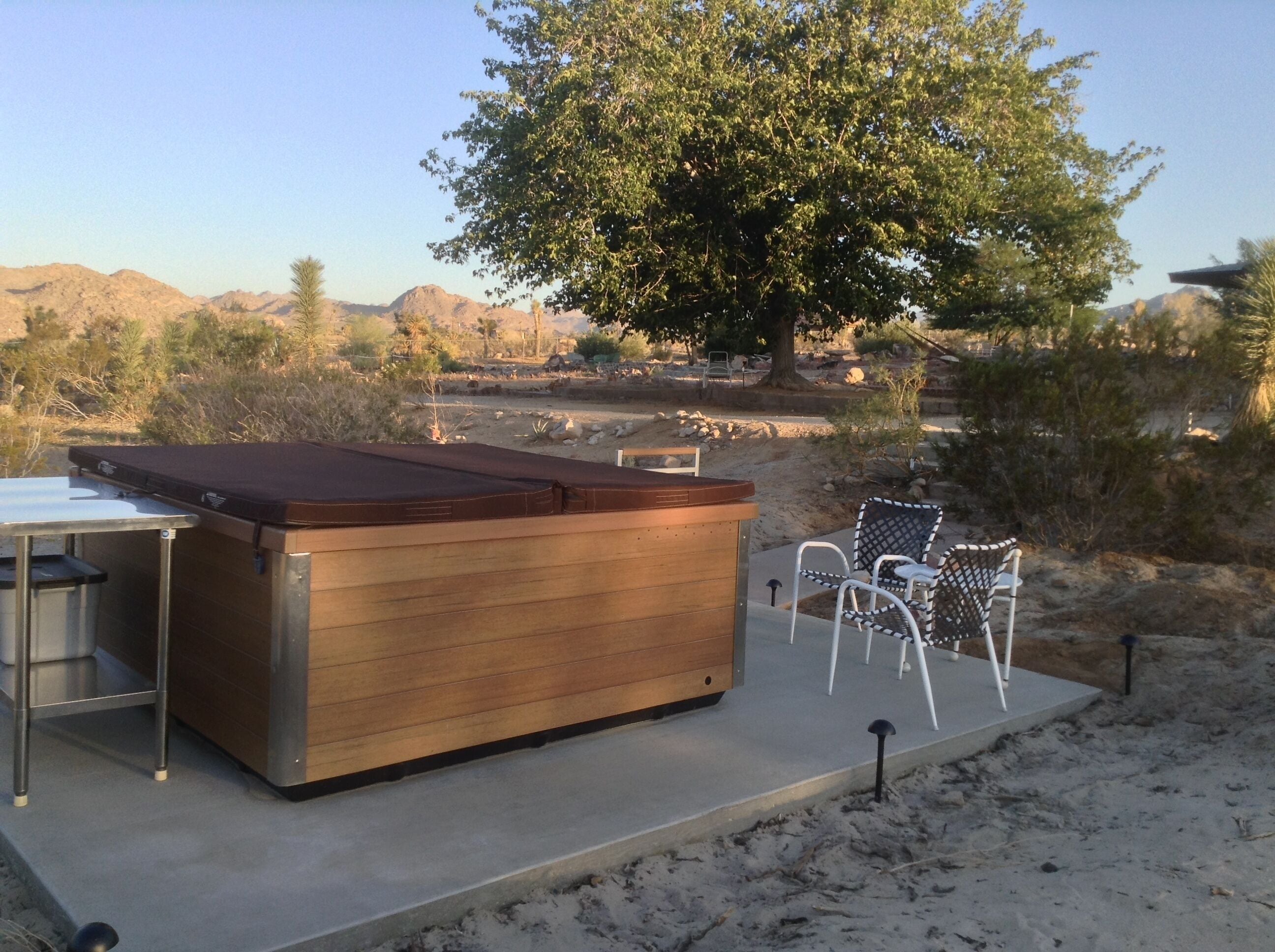 A hot tub with a wooden exterior and metal frame, surrounded by a patio area with chairs and a table.