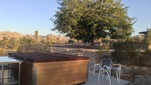 Un bain à remous avec une structure extérieure en bois et un cadre en métal, entouré d’un espace patio aménagé avec des chaises et une table.
