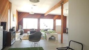 Un grand espace de vie comprenant un canapé, un fauteuil, une petite table et un coin cuisine équipé d’appareils électroménagers.