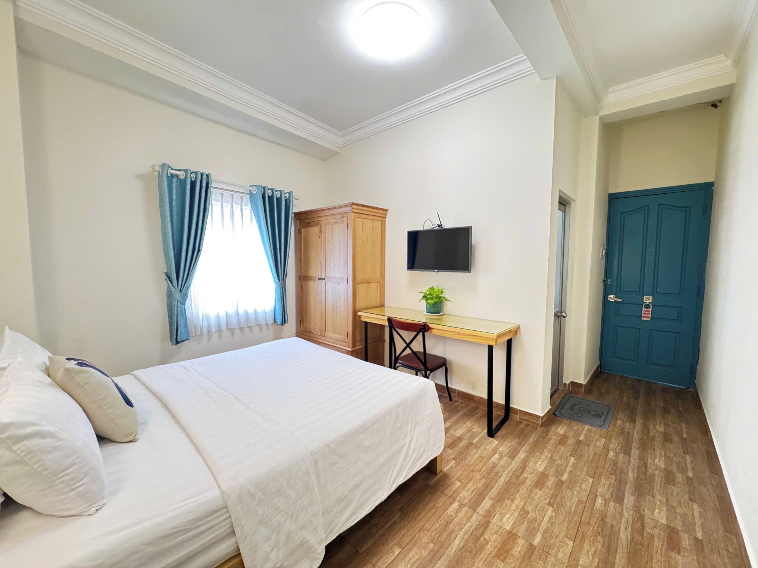 Un dormitorio con cama, escritorio, silla, armario, televisor y puerta.