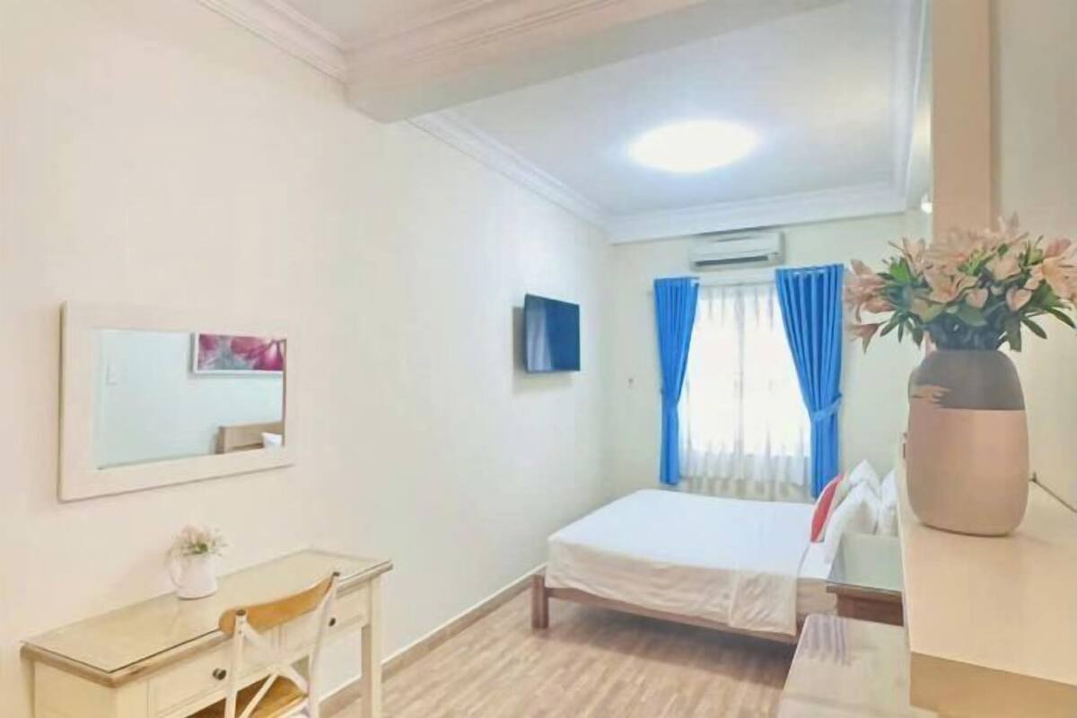 Ein Hotelzimmer mit Bett, Schreibtisch, Stuhl, Spiegel, einem an der Wand befestigten Fernseher und einem Fenster mit Vorhängen.