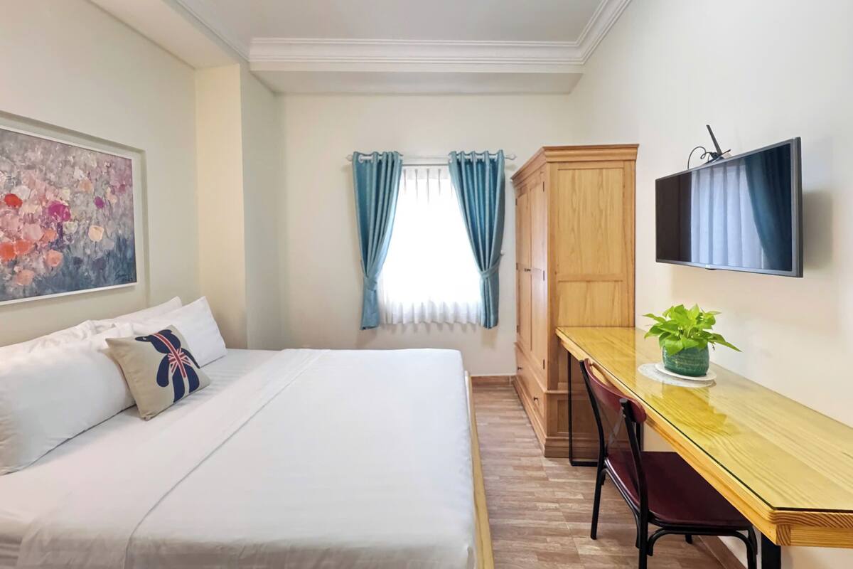 Ein Schlafzimmer mit Bett, Schreibtisch, Stuhl, Fernseher, Kleiderschrank und einem Fenster mit Vorhängen.