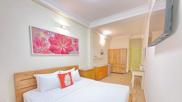 Un dormitorio con cama, armario de madera, escritorio y un cuadro grande con motivos florales en la pared.