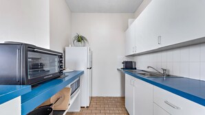 A compact kitchen with a toaster oven, a white refrigerator, a sink, and a blue countertop. - Ocean Views 49 (Airlie Beach)