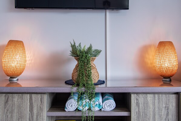 A modern room with a wooden shelf displaying rolled towels and a woven vase with greenery. - Ocean Views 49 (Airlie Beach)
