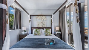 A hotel room with a large bed, a macrame wall hanging, and a view of palm trees. - Ocean Views 49 (Airlie Beach)
