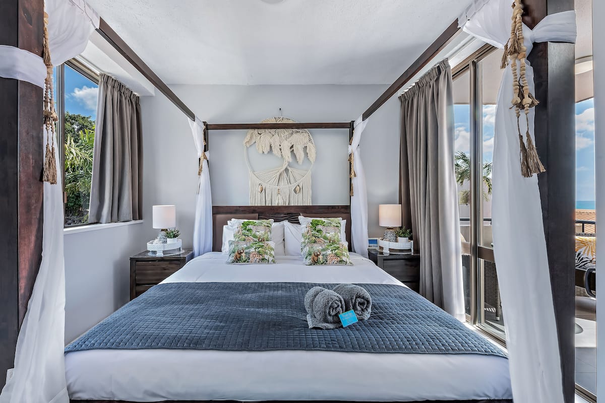 A hotel room with a large bed, a macrame wall hanging, and a view of palm trees.