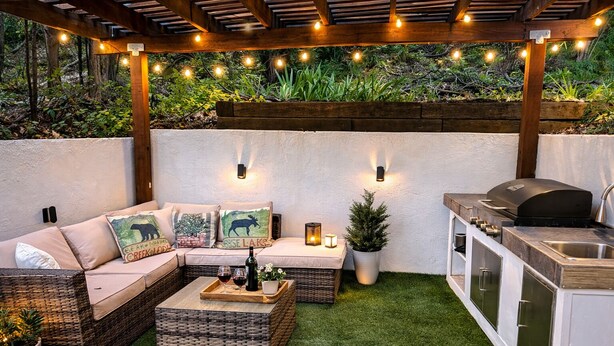 An outdoor patio with a wicker sofa, a small table with a bottle and glasses, a grill, and string lights. - A cabin with beautiful mountain views and outdoor lounge (Dunsmuir)
