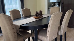 A dining area with a dark wooden table, beige upholstered chairs, a woven placemat, and a decorative pine cone centerpiece. - A cabin with beautiful mountain views and outdoor lounge (Dunsmuir)