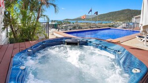 A hot tub with a view of a pool and mountains in the background. - Ocean views 27A (Airlie Beach)