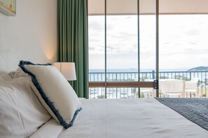 A hotel room with a bed, a view of the sea, and a balcony with chairs. - Ocean views 27A (Airlie Beach)