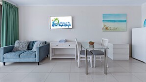 A modern living room with a sofa, a glass dining table, and a white cabinet. - Ocean views 27A (Airlie Beach)