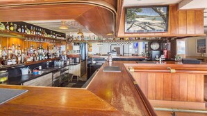 A bar area with wooden bar tops, a variety of bottles on shelves, and a large painting above the bar. - Ocean views 27A (Airlie Beach)