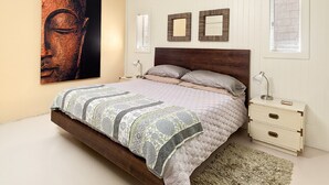 Un dormitorio con cama, mesitas de noche, un cuadro grande en la pared y dos espejos.
