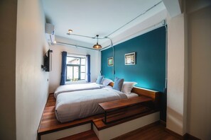 Una habitación con dos camas, un banco de madera, una ventana con cortinas y una lámpara en el techo.