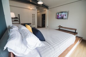 Una cama bien hecha con almohadas blancas y azules, un banco de madera y un televisor en la pared.