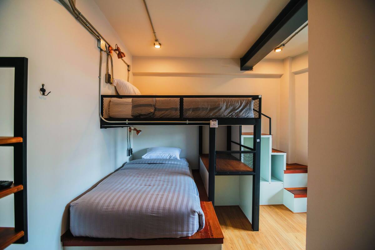 A bunk bed room with a wooden floor, a white wall, and a staircase.