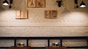 Ein Restaurant mit freiliegenden Backsteinwänden, Holztischen und hängenden Pendelleuchten.