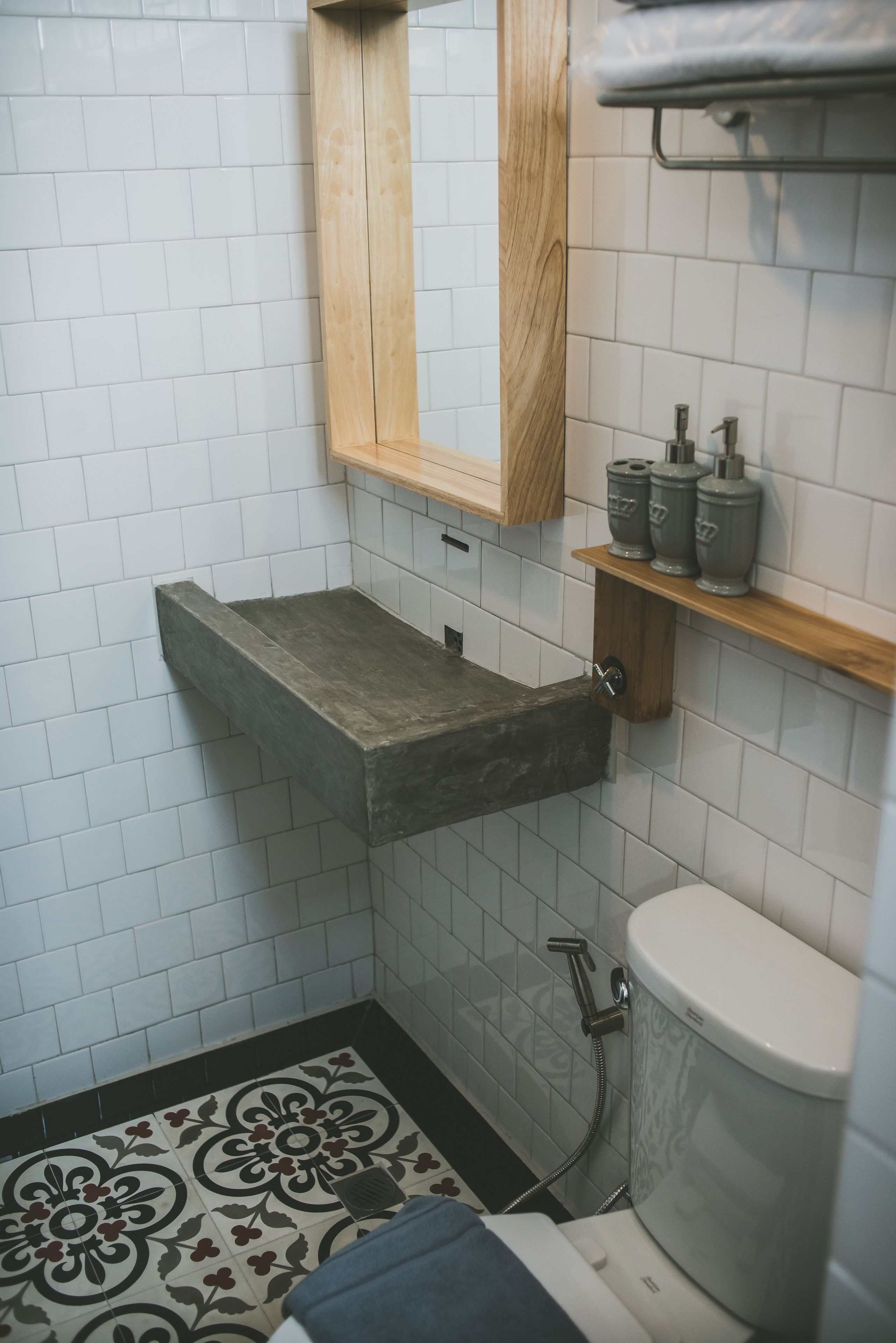 Een badkamer met een witte betegelde vloer, een houten medicijnkastje, een betonnen wastafel en een toilet.