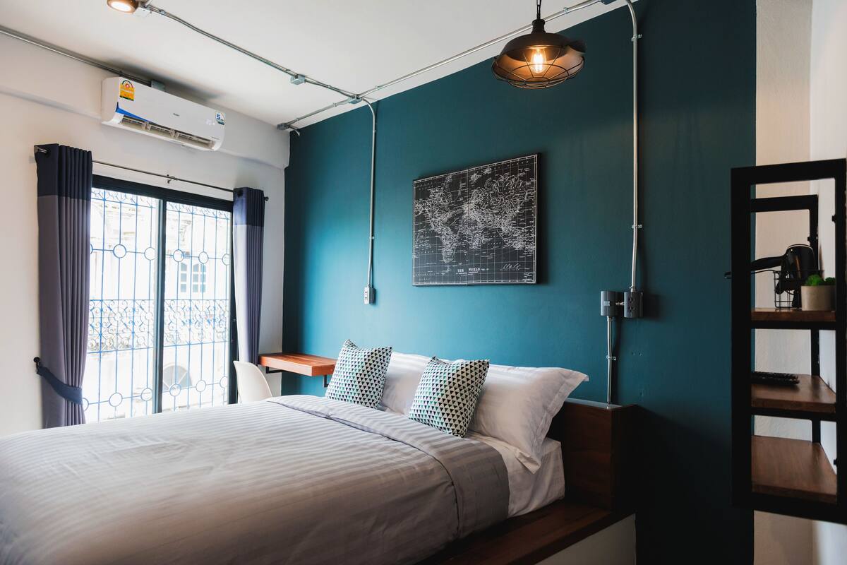 A bedroom with a bed, a map on the wall, a desk, and a window with curtains.
