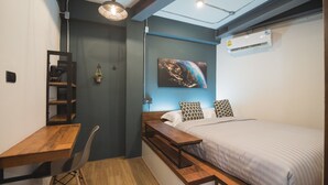 Ein kleines Schlafzimmer mit einem Bett, einem Schreibtisch, einem Stuhl, einer Pendelleuchte und einer Wand-Klimaanlage.