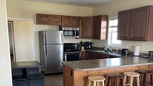 A modern kitchen with wooden cabinets, stainless steel appliances, a granite countertop, and a bar stool area. - Looking for a cozy getaway? This country property is perfect!  (Weldon)
