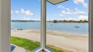 A view from a window overlooking a beach with boats, a clear sky, and distant hills. - BAYFRONT! AUGUST 8 - 10 OPEN AMAZING VIEWS & LOCATION WALK TO FOOD, SHOPS, OCEAN (San Diego)