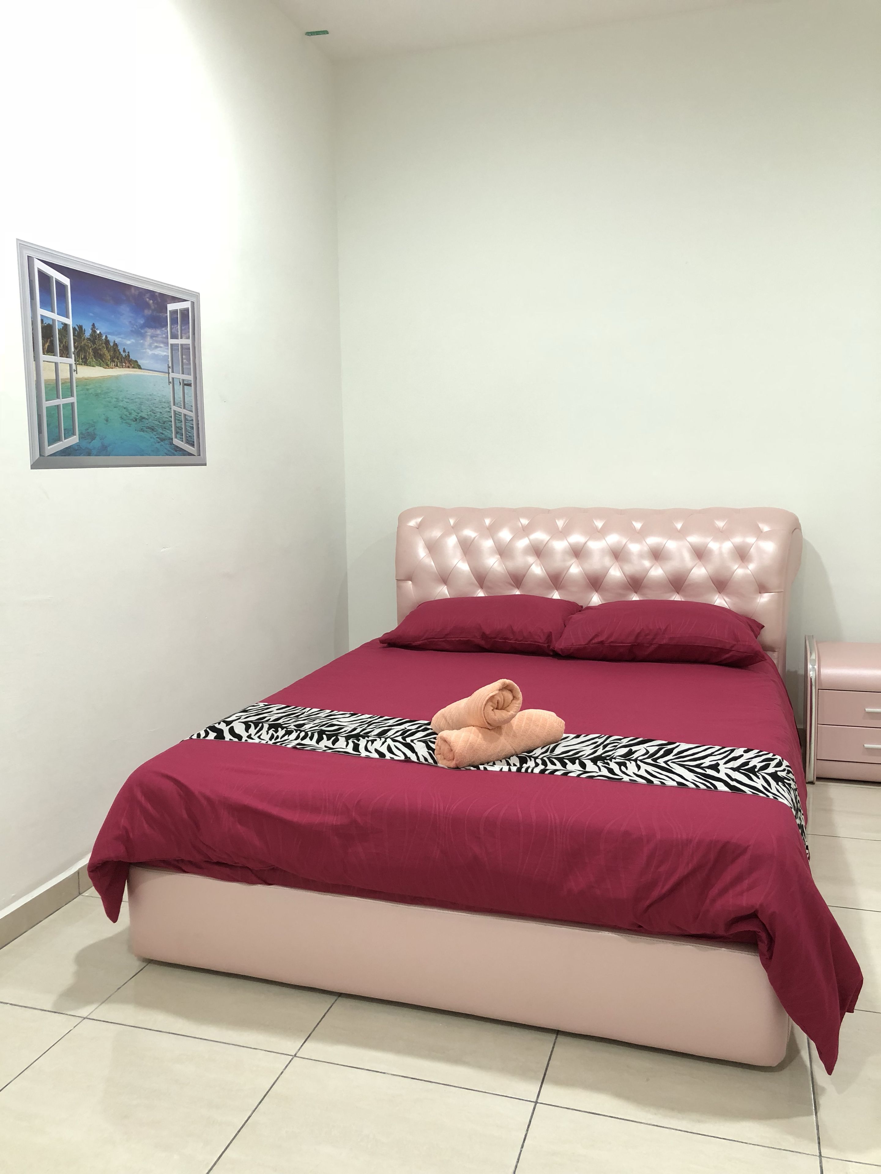 A neatly made bed with a pink headboard, a zebra-patterned bedspread, and a pair of rolled towels.