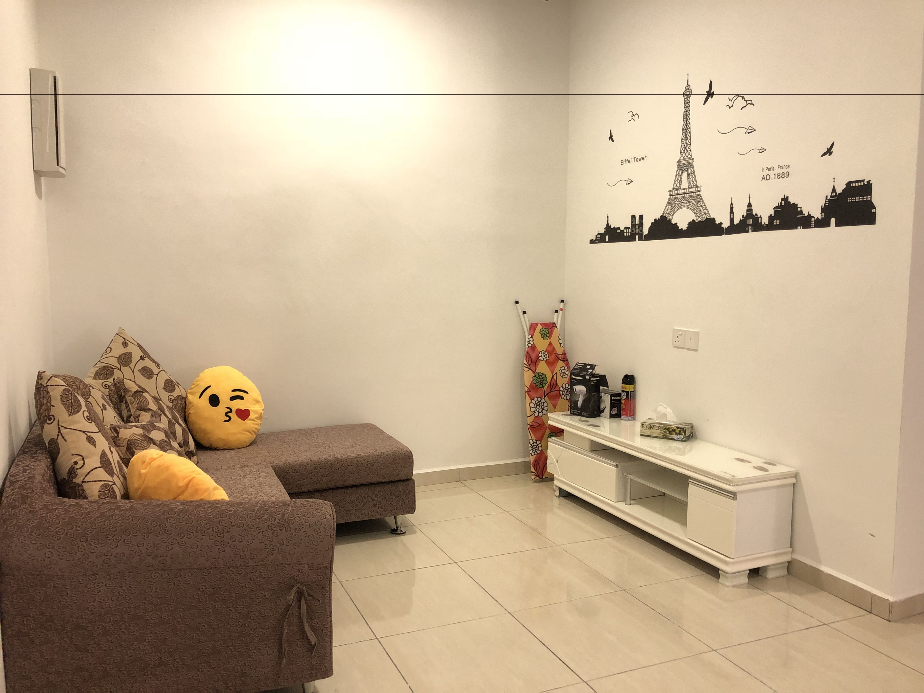 Un salón con sofá, cojines, una mesa de centro y una decoración en la pared con la Torre Eiffel.