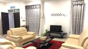 A living room with two beige sofas, a red rug, a TV on a stand, and a sign reading "KELUAR". - Langkawi Shell Out Villa (Langkawi)