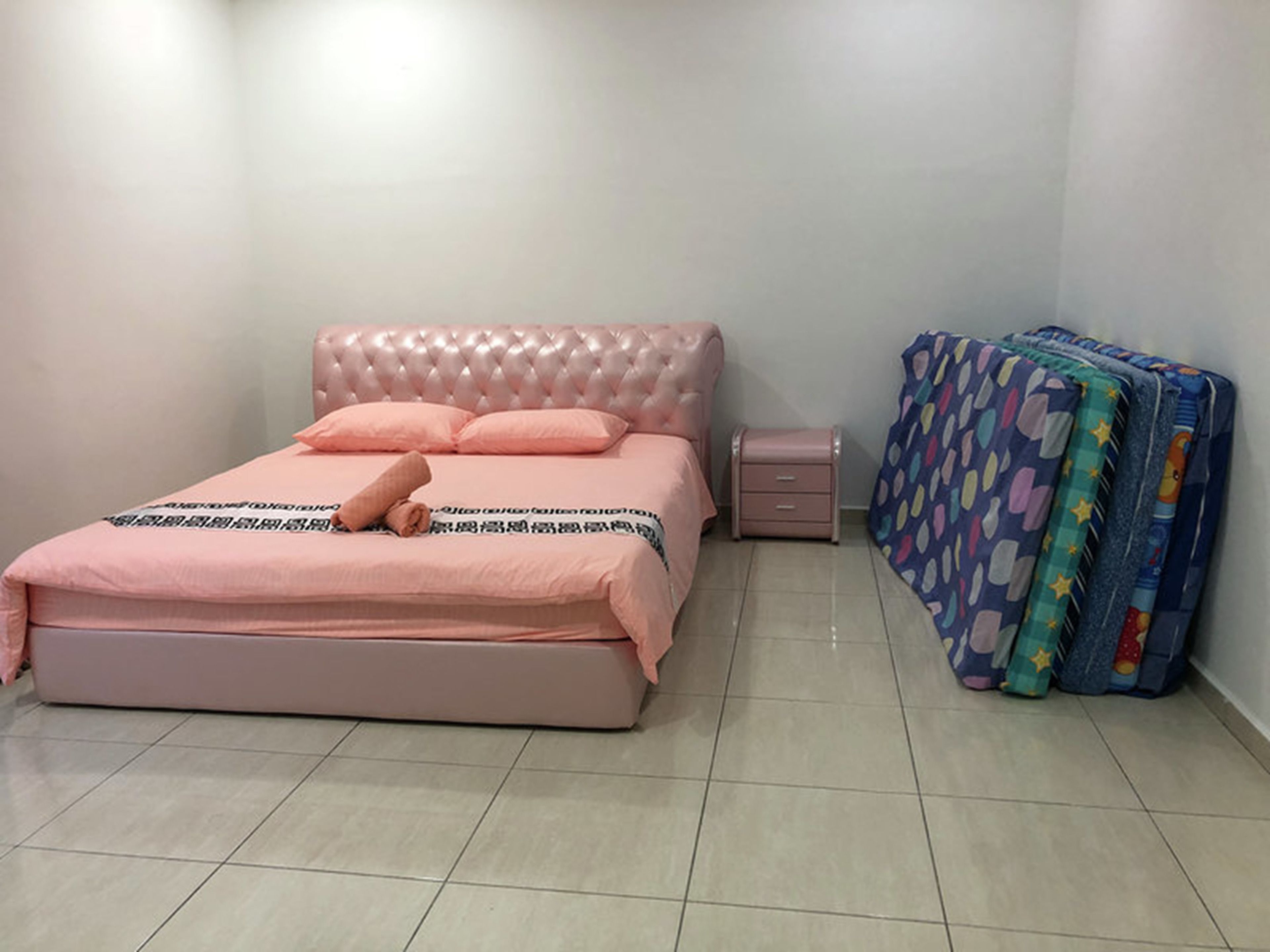 A bedroom with a pink bed, a bedside table, and a colorful mattress.