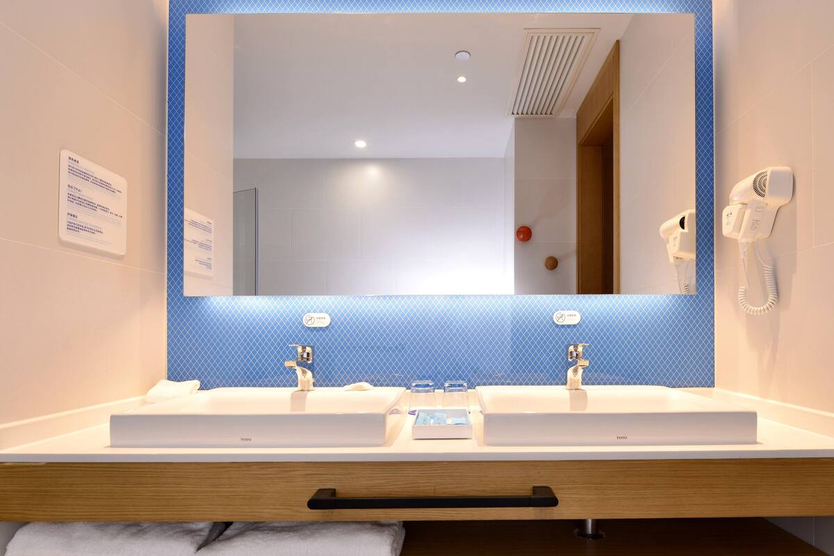 A modern bathroom with a large mirror, two sinks, a towel rack, and a hairdryer.