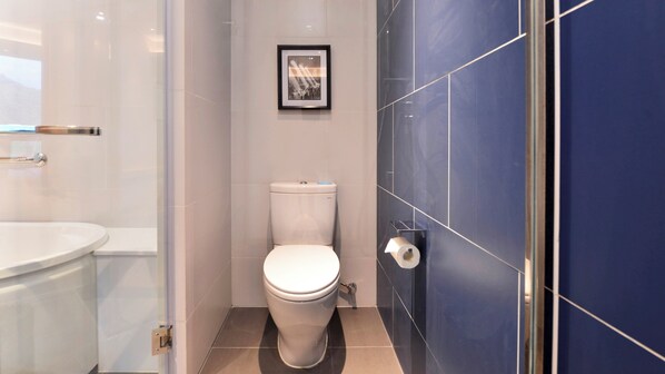 Un baño moderno con inodoro, un cuadro en la pared y una zona de ducha con azulejos azules.