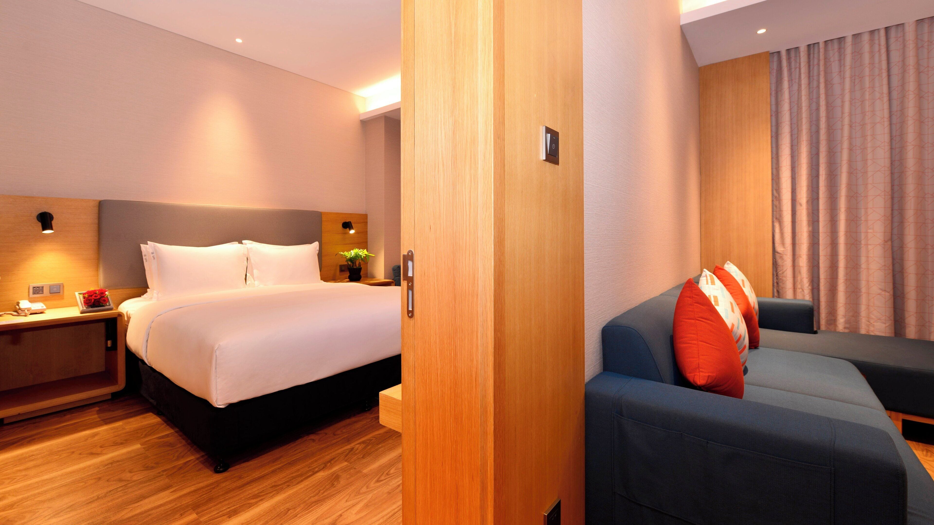 Una habitación de hotel con cama, mesita de noche, sofá y cortina.