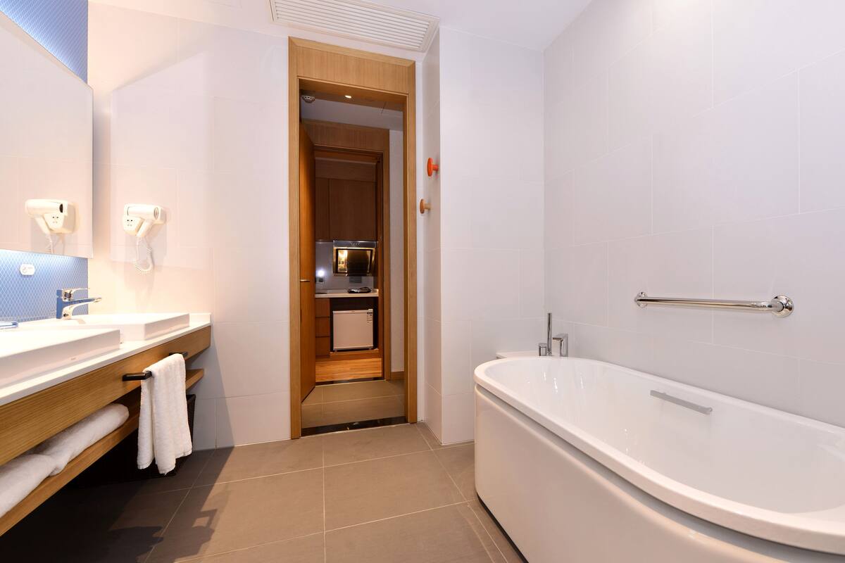 A modern bathroom with a large bathtub, a sink with a mirror, and a small refrigerator.