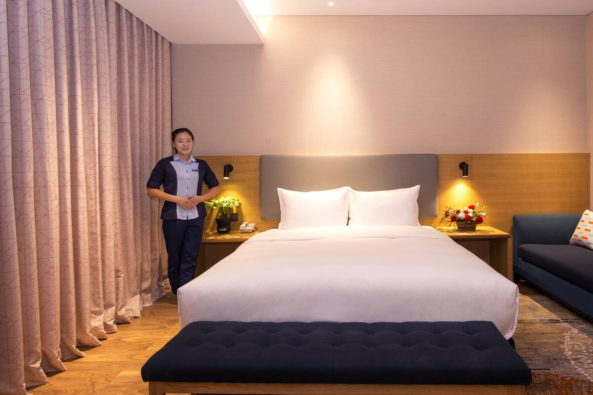 A hotel room with a large bed, bedside tables with lamps, a sofa, and a bench.