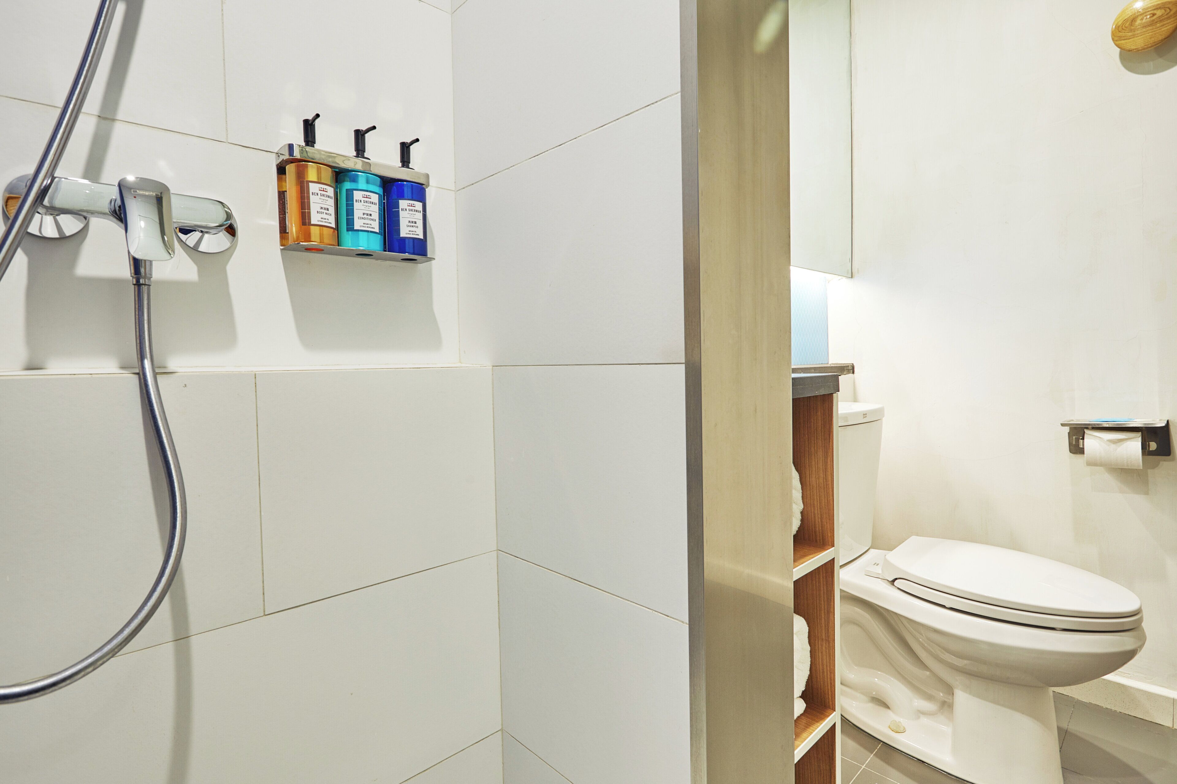 Un baño con ducha, inodoro y un estante con artículos de tocador.