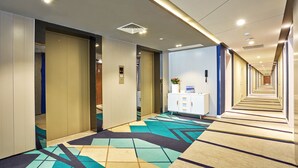 A hotel corridor with a patterned carpet, a reception desk, and a long hallway leading to rooms.