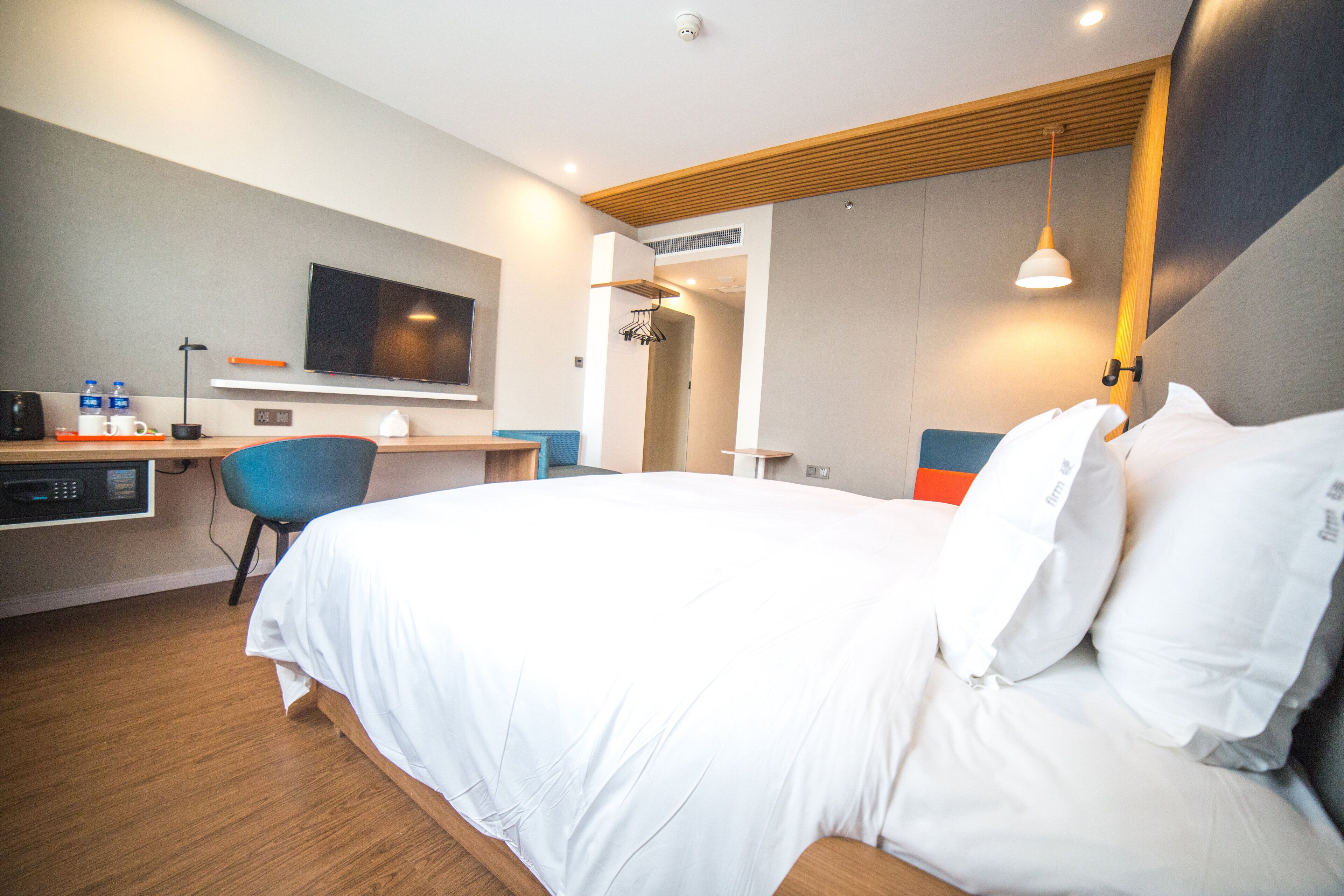 Una habitación de hotel con cama, escritorio, silla, televisor y espejo.