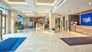 A spacious lobby with a marble floor, a reception desk, and a staircase leading to upper floors.