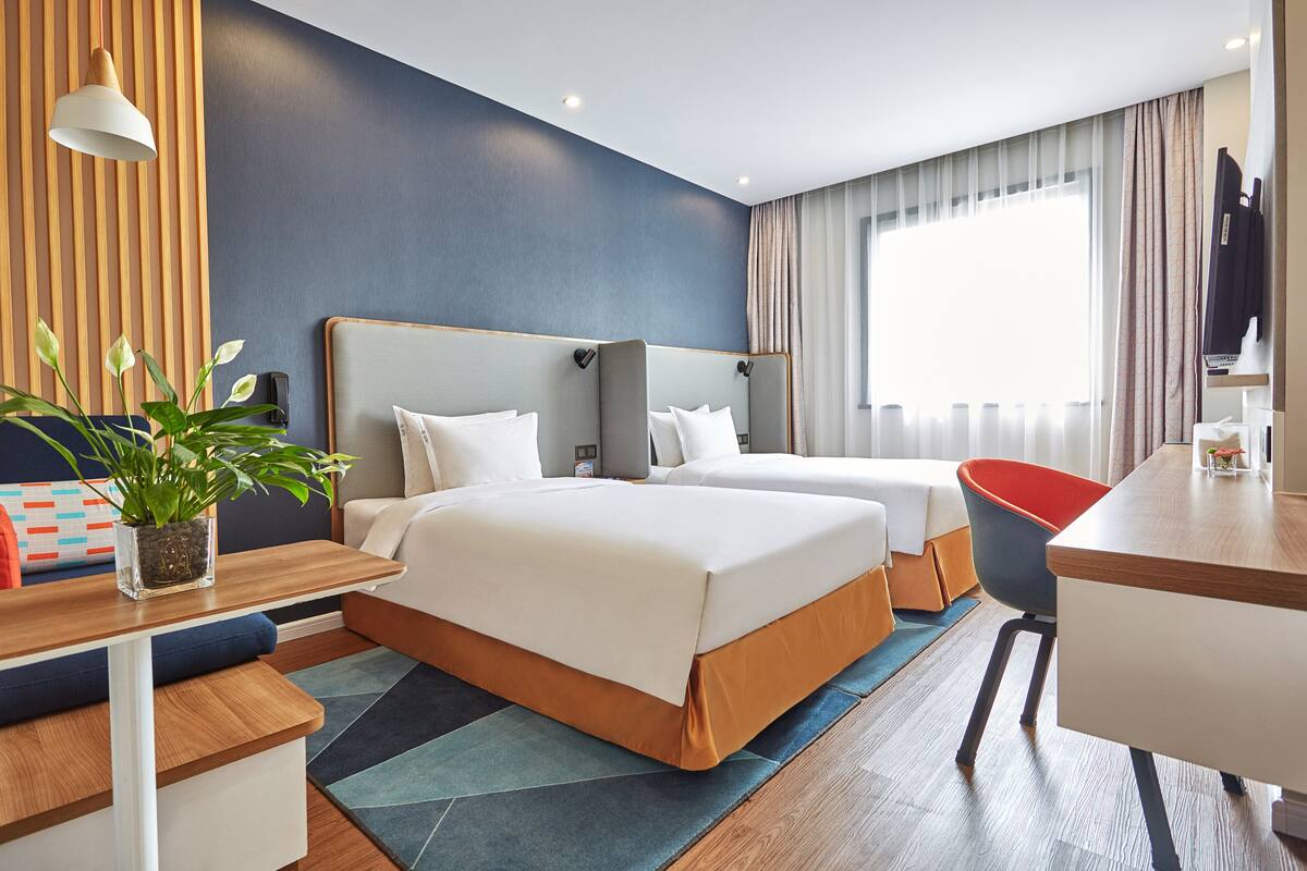Ett hotellrum med två sängar, ett skrivbord, en stol, en tv och en krukväxt.
