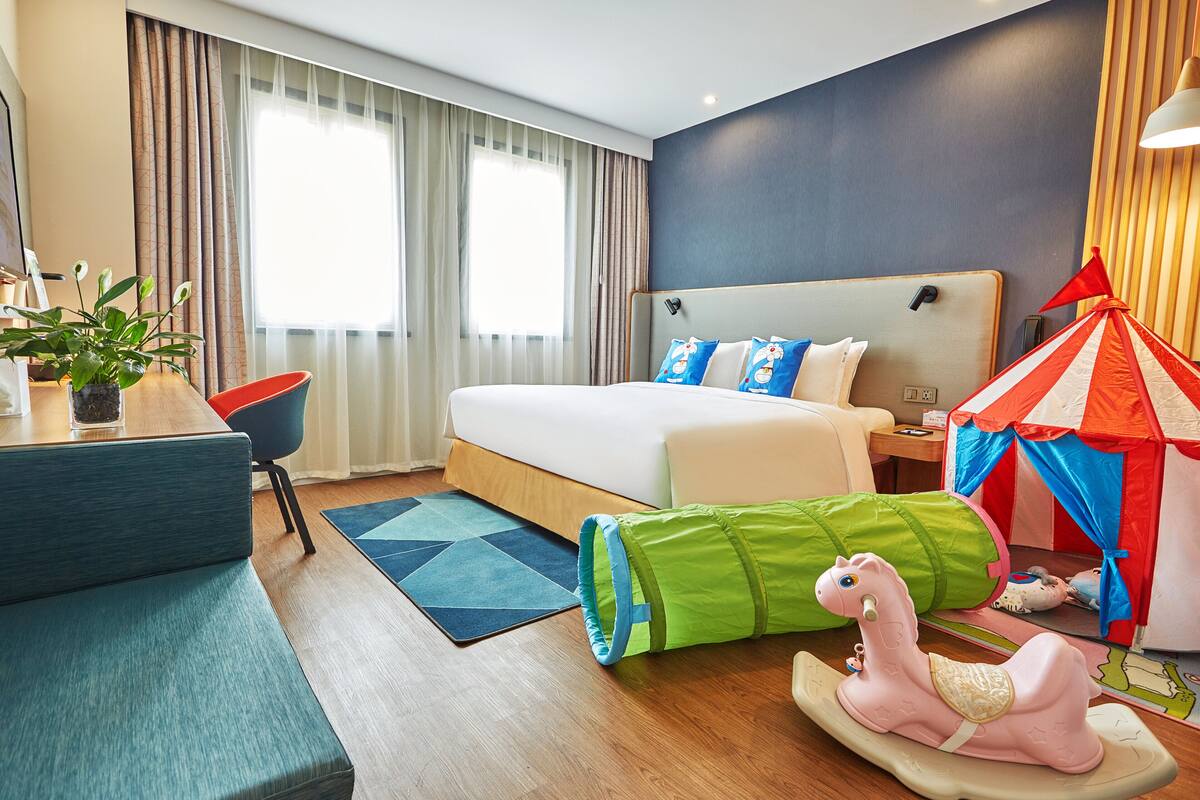 Ett hotellrum med en säng, ett skrivbord, en stol, ett tält och en leksakshäst.