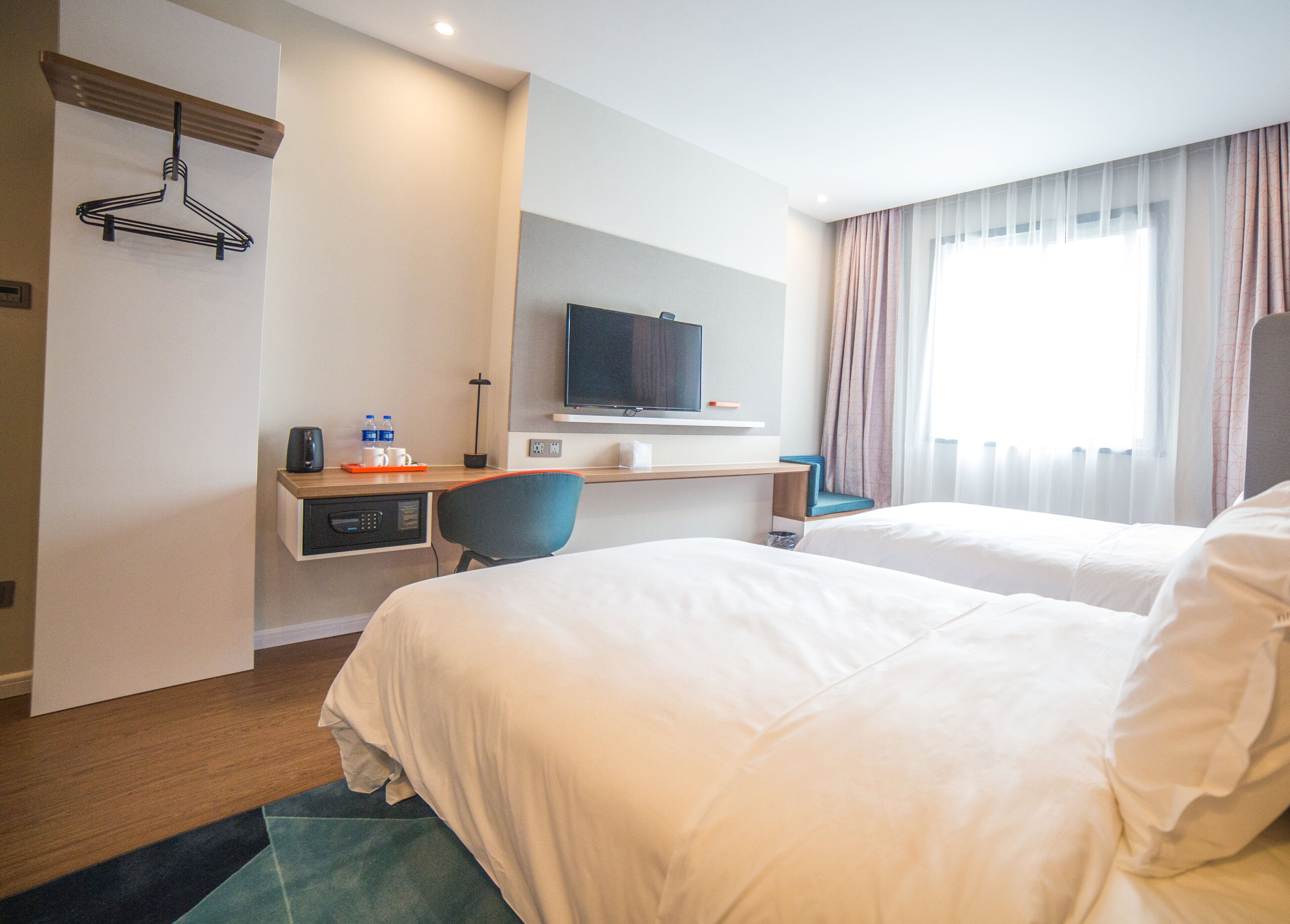 A hotel room with two beds, a desk with a chair, a TV, and a window with curtains.