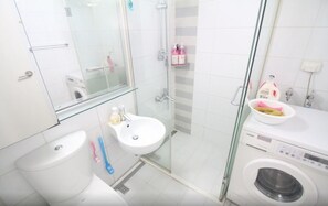 A modern bathroom with a toilet, sink, glass shower enclosure, and a washing machine. - GANGNAM SK Metro A (Seoul)
