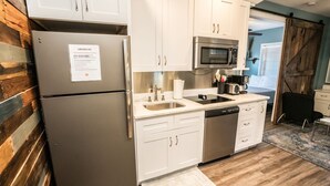 A modern kitchen with white cabinets, stainless steel appliances, and a wooden accent wall. - Inn The Heights - Apt. 9 (Tampa)