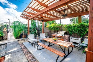 An outdoor patio with a wooden pergola, a barbecue grill, and a dining table with chairs.